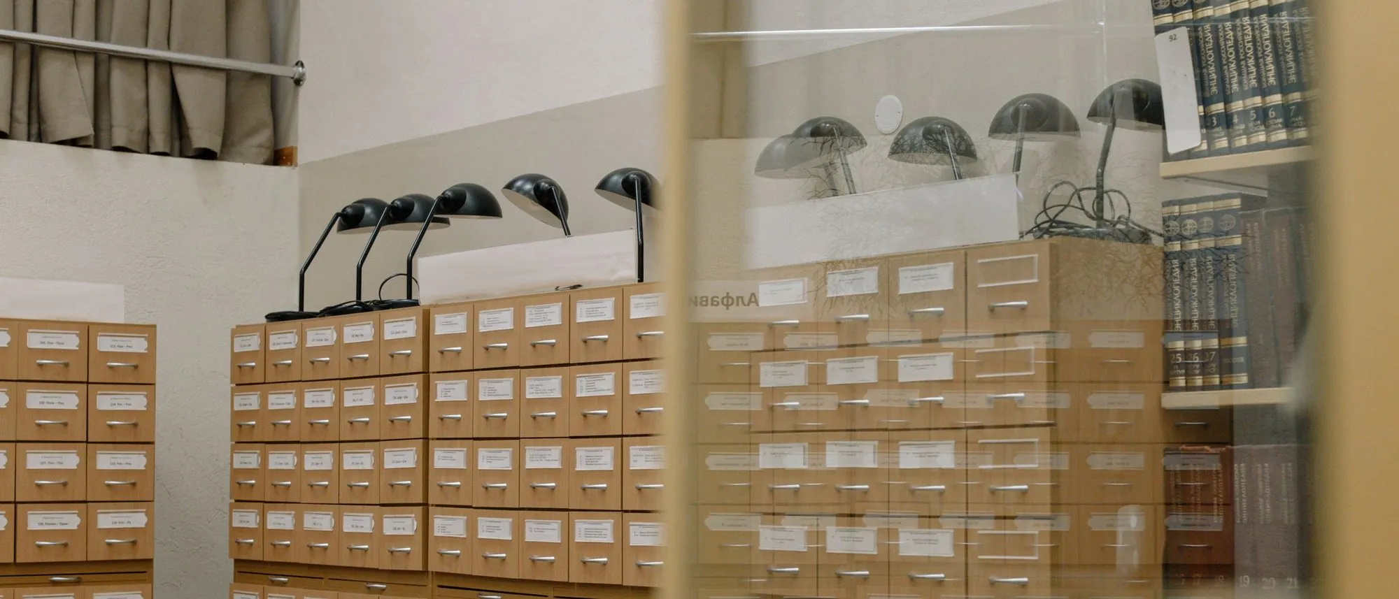 Rows of small wooden catalogue drawers beneath a pair of classic desk lamps.