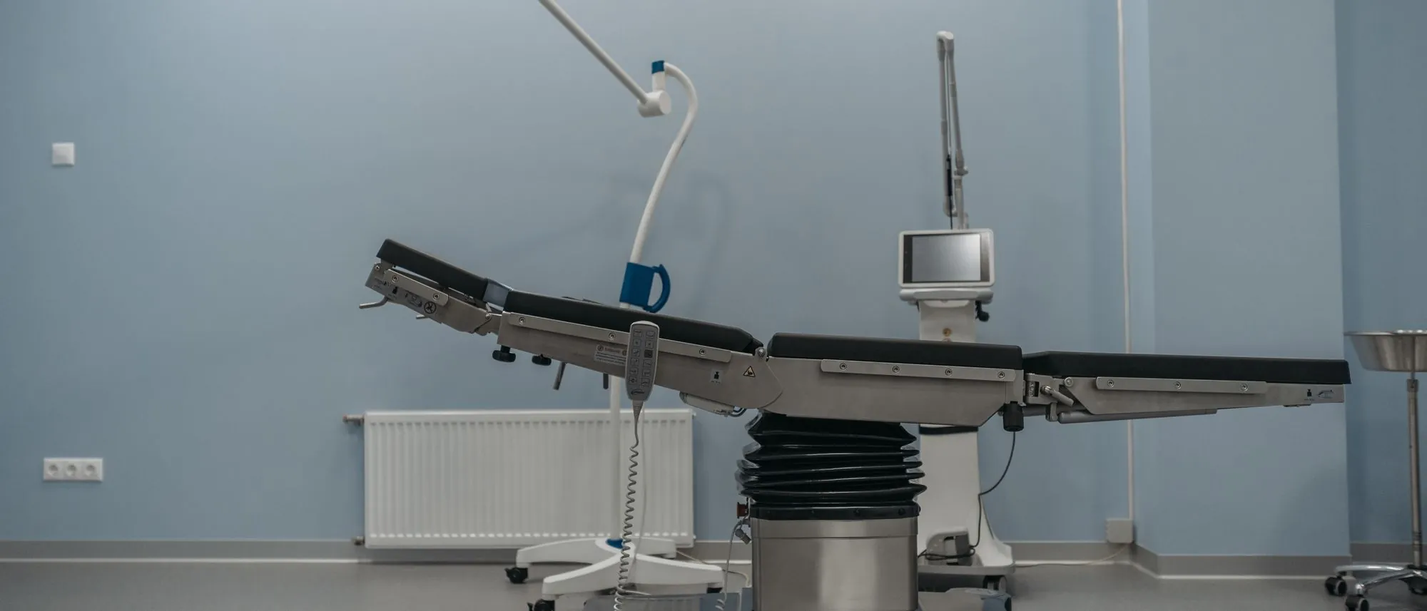 An empty operating table under a surgical lamp in a pale blue room