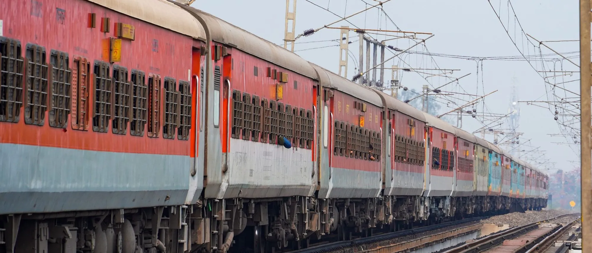 A long passenger train runs along elevated tracks in India.