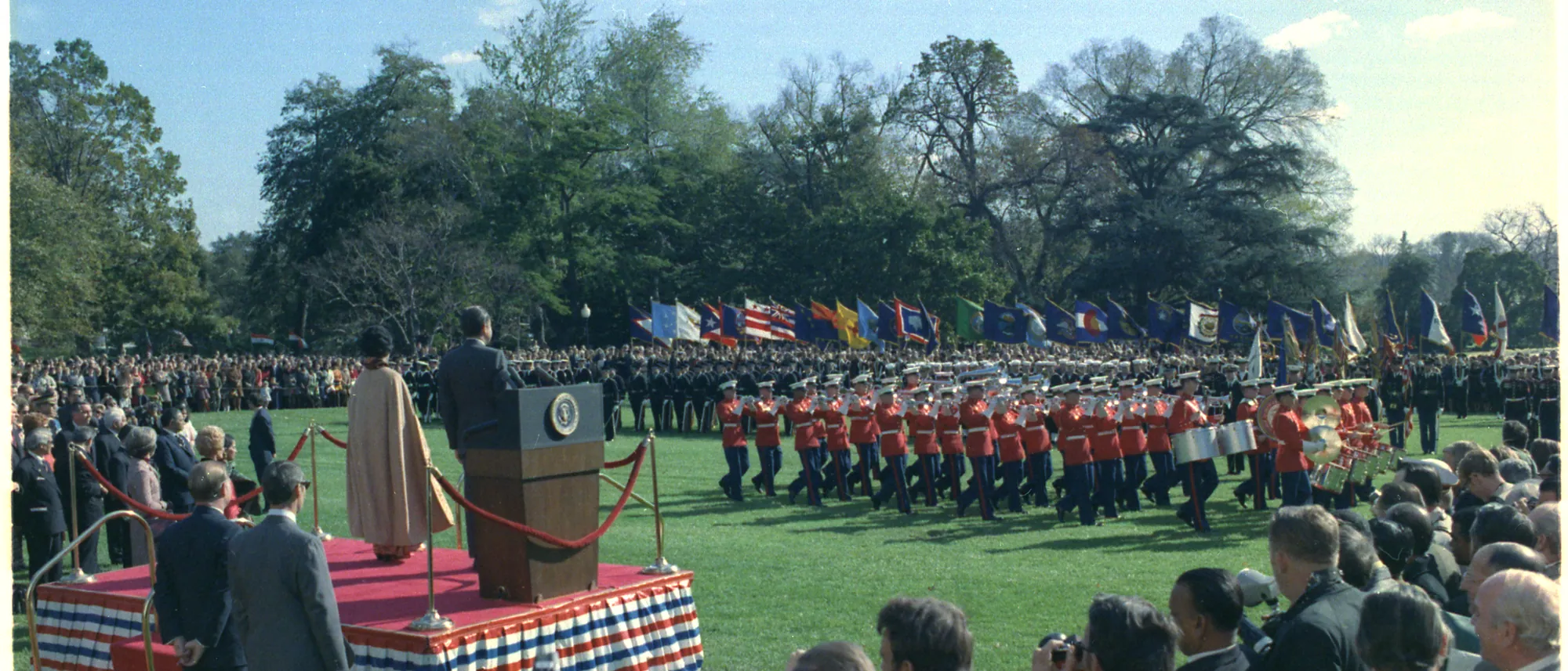 Indira Gandhi and Richard Nixon seen from behind on the podium as a marching band passes on the South Lawn of the White House, 4 November 1971