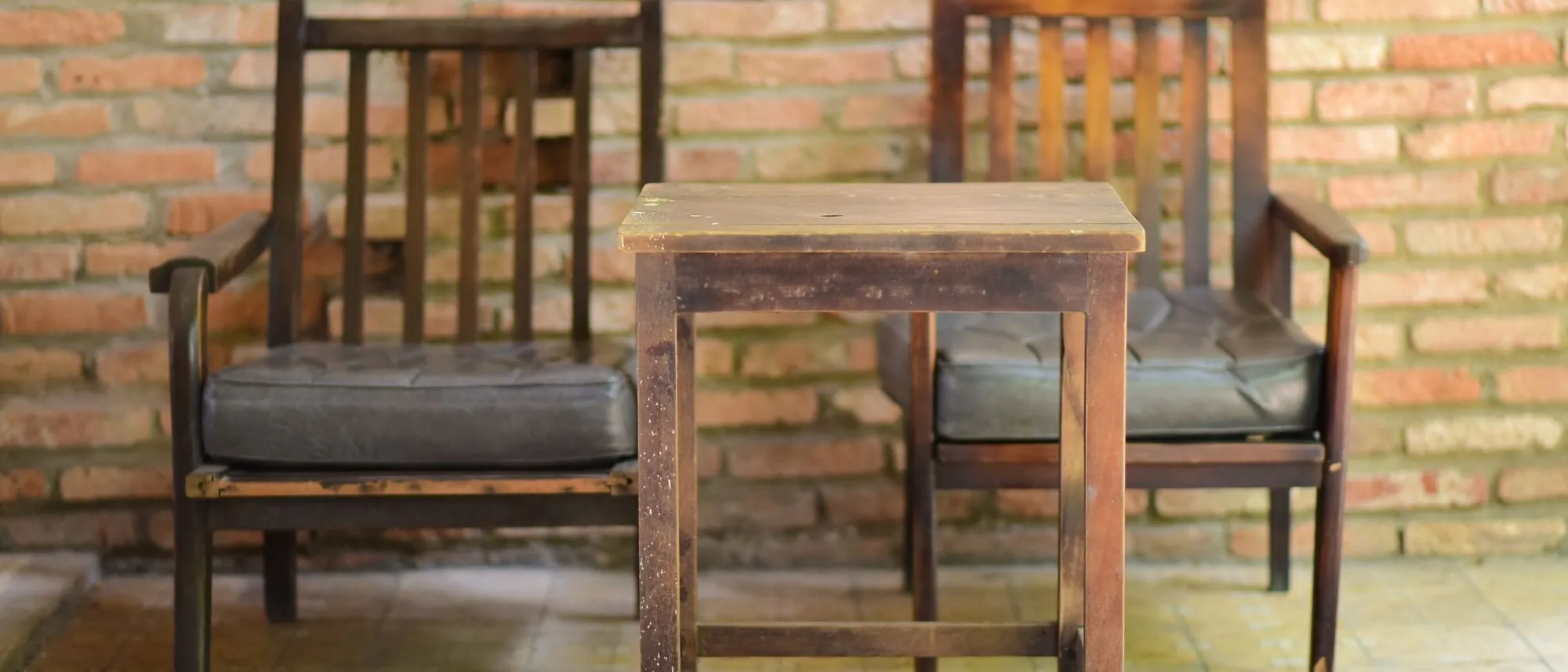 Wooden chairs and a small table set against a bare brick wall.