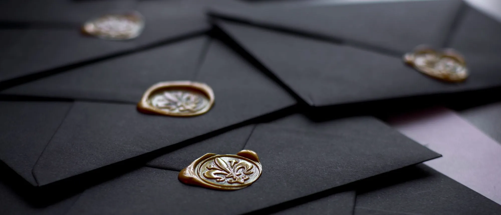 Black envelopes closed with wax seals lie together in close-up.