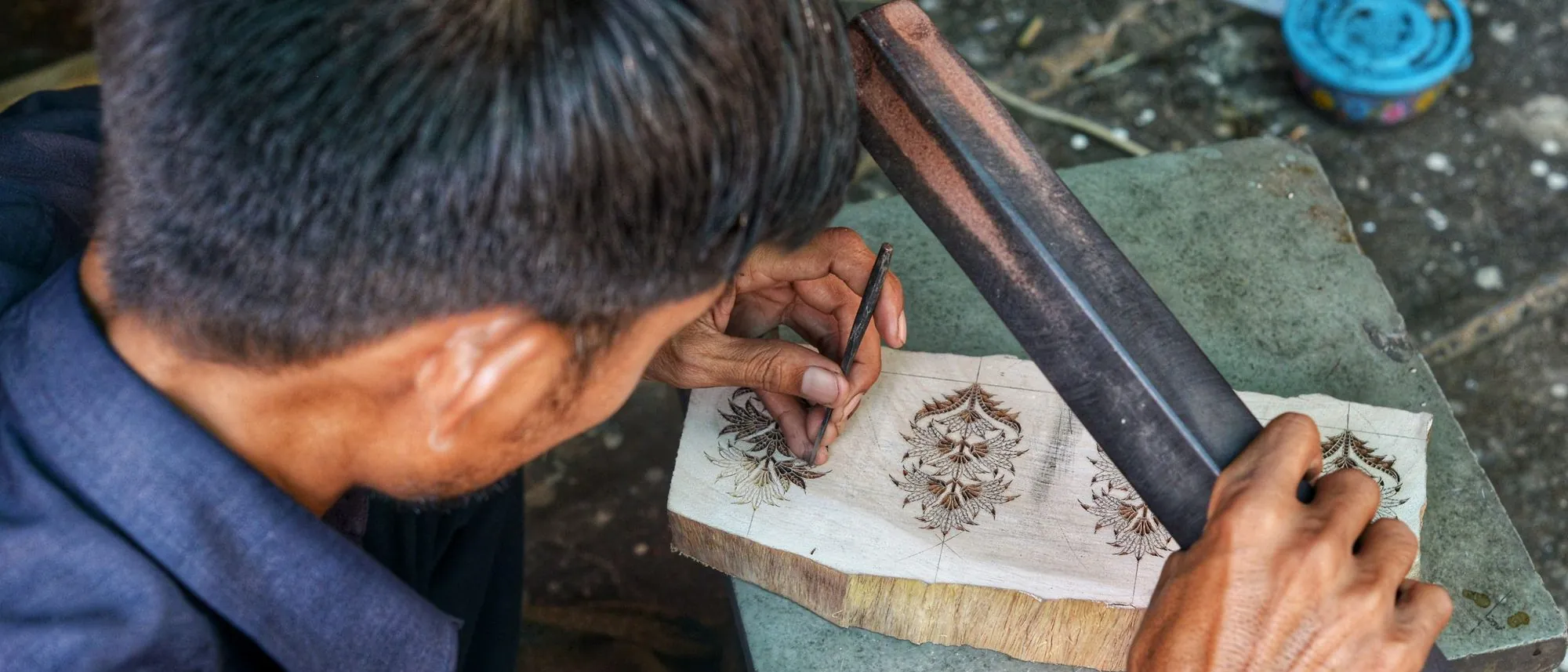 An artisan's hands carve a wooden textile printing block in a Jaipur workshop.