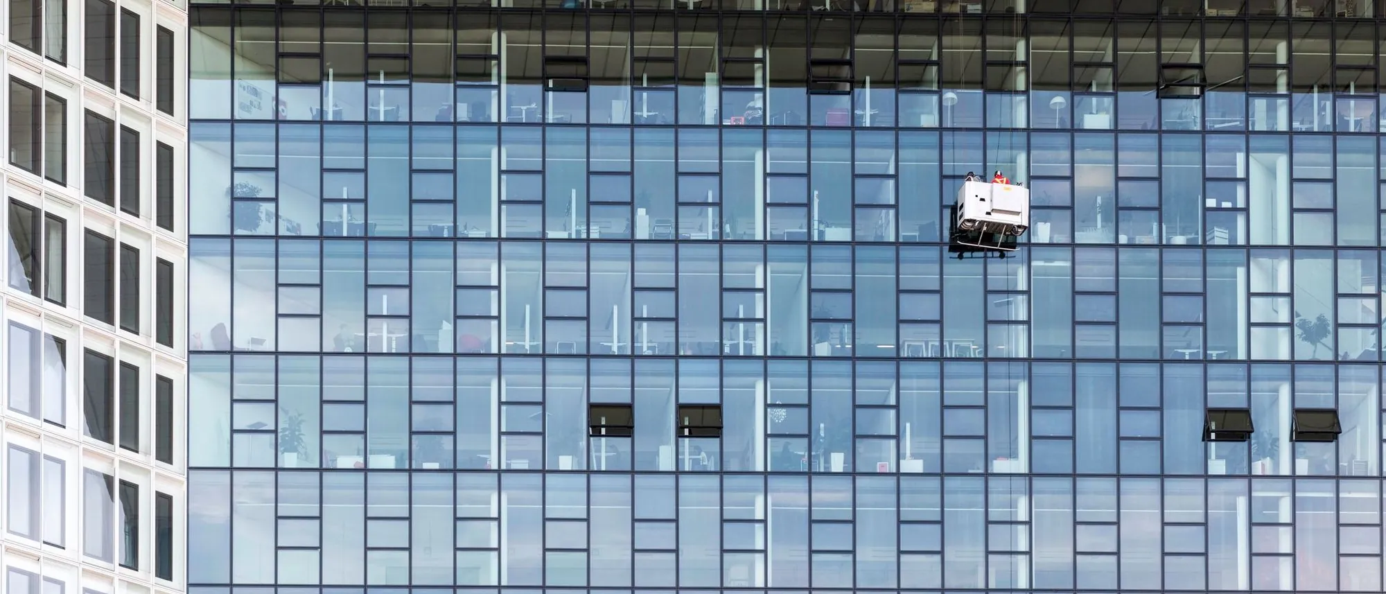 Two window cleaners on ropes, small against the glass facade of a high-rise office building.