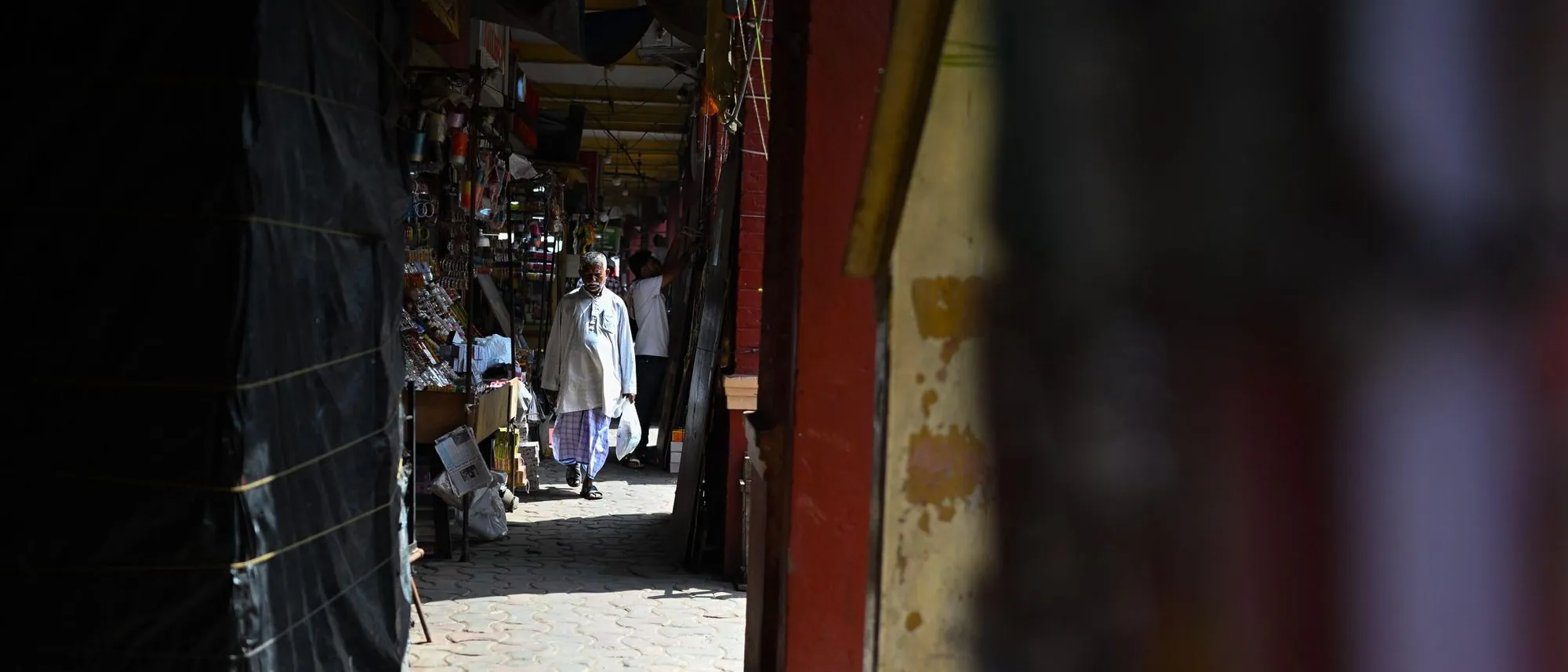 A man walks through a market alley in Kolkata lined with stalls.