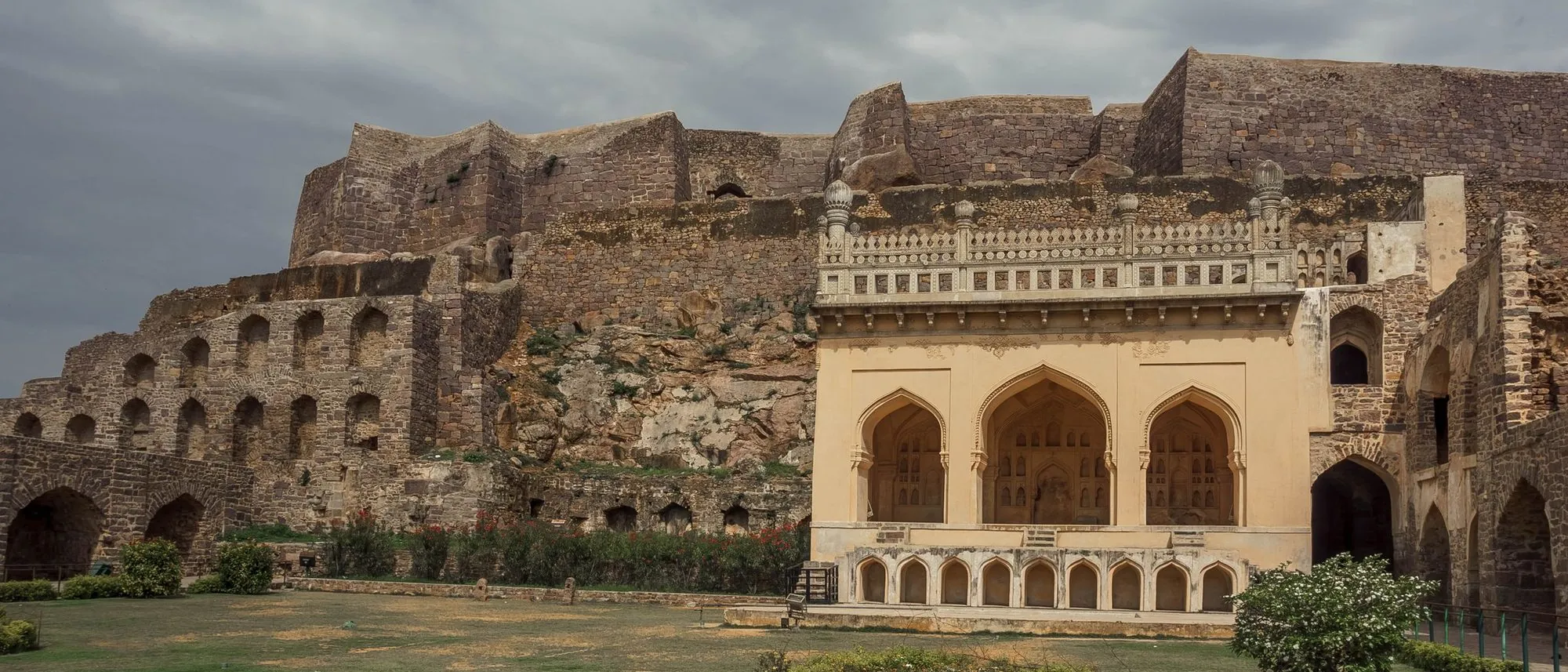 The stone ramparts and arched pavilions of Golconda Fort in Hyderabad stand under a grey sky.