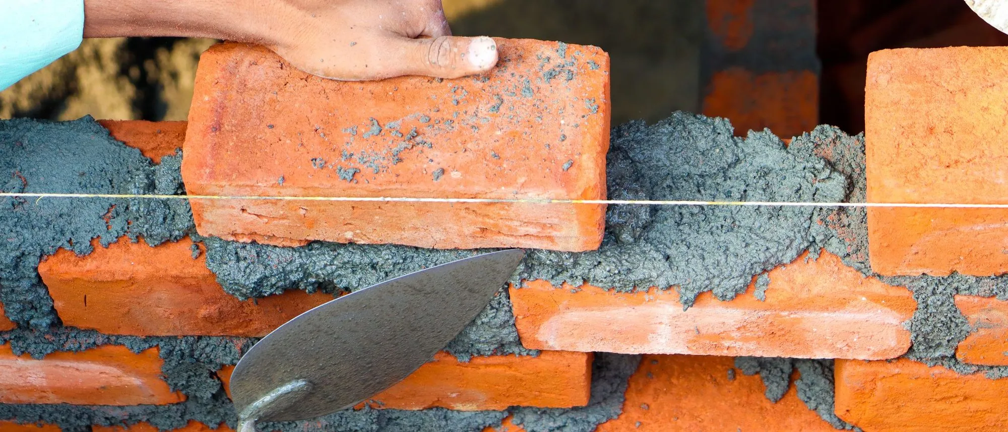 Hands set a brick into wet cement on a half-built wall.