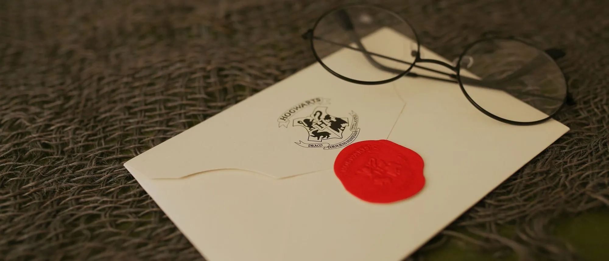 A white envelope closed with a red wax seal lies beside a pair of eyeglasses on a textured surface.