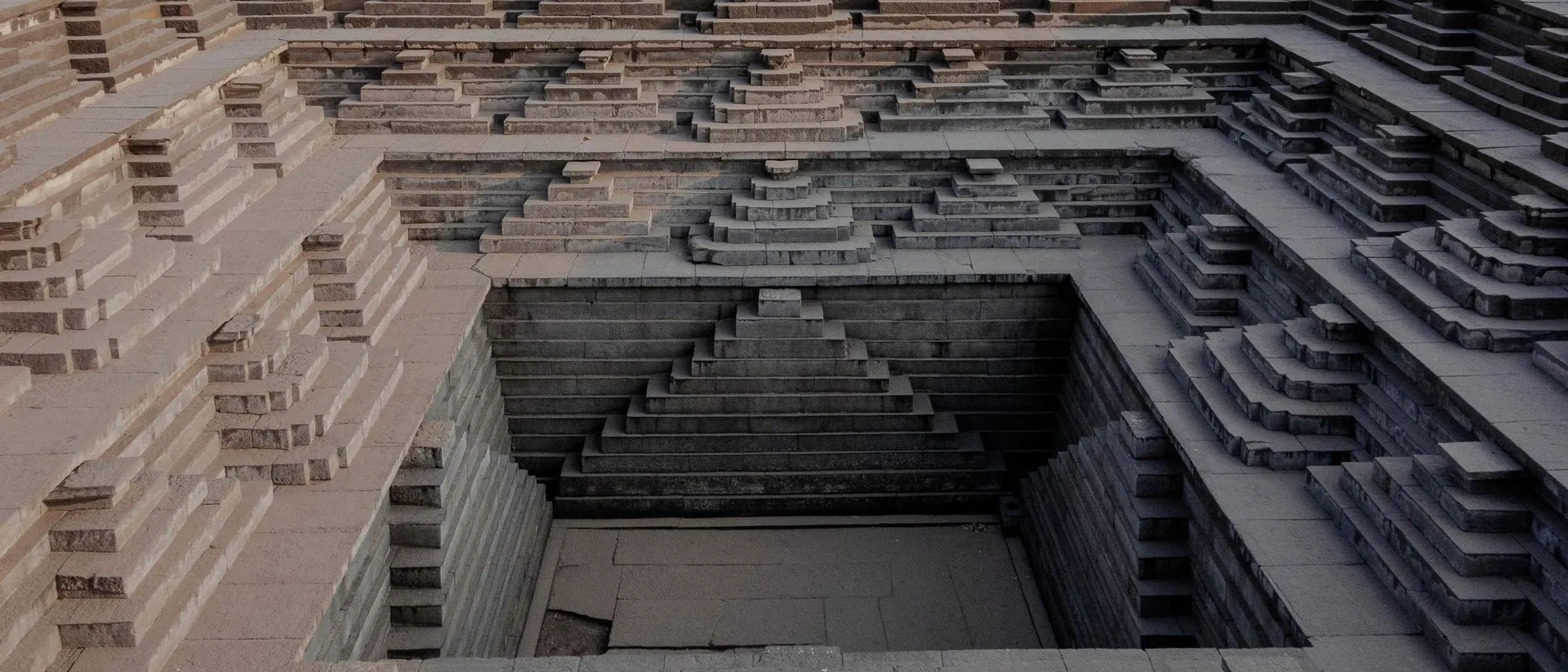 The symmetrical stone steps of an ancient stepwell in Hampi descending towards the water.