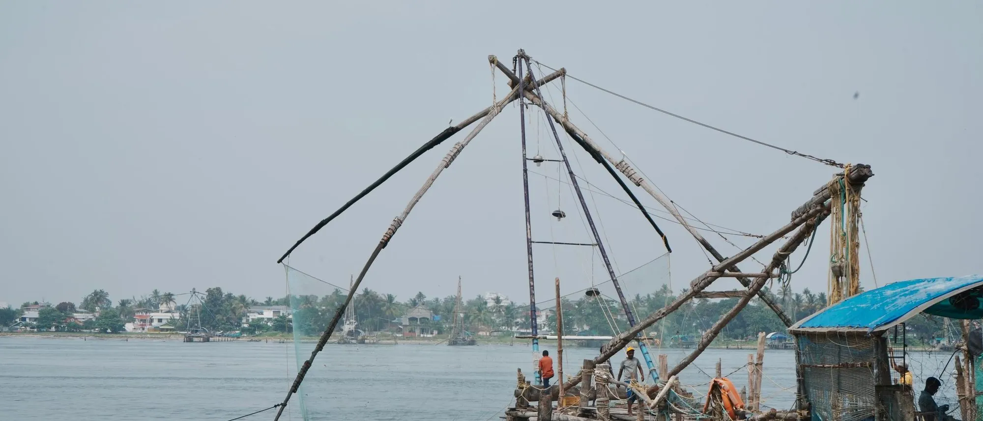 Chinese fishing nets stand over the water at Kochi while fishermen work on the shore.