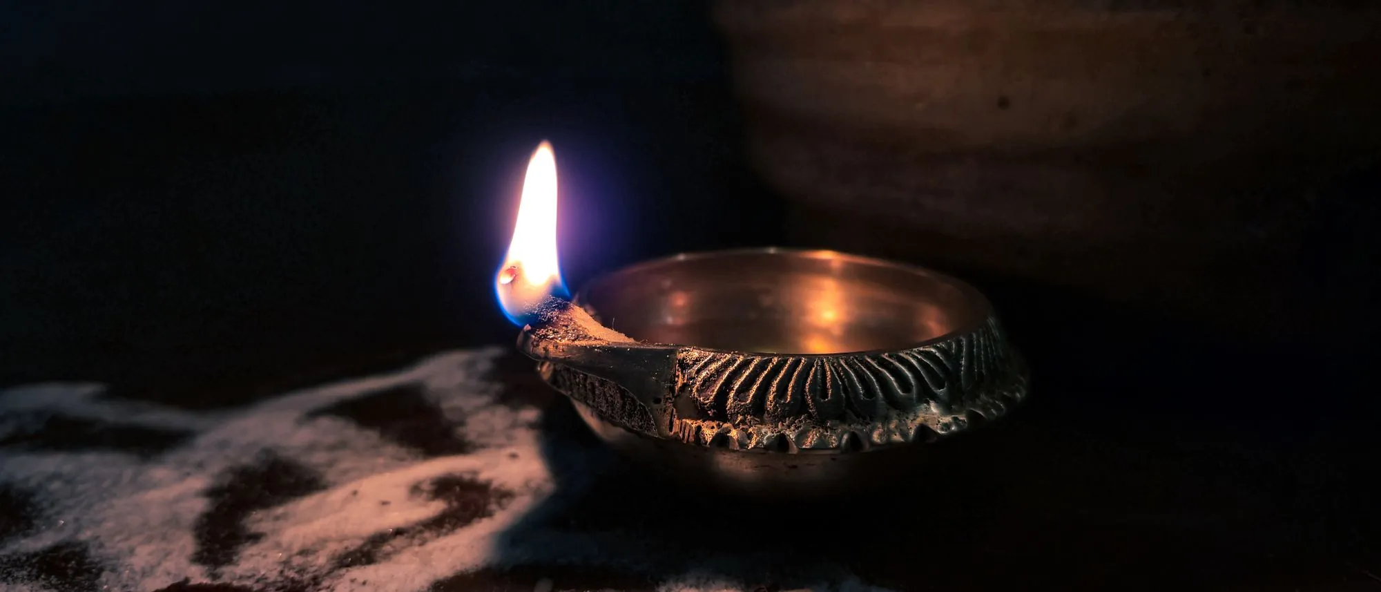 A single lit brass diya lamp on a dark floor