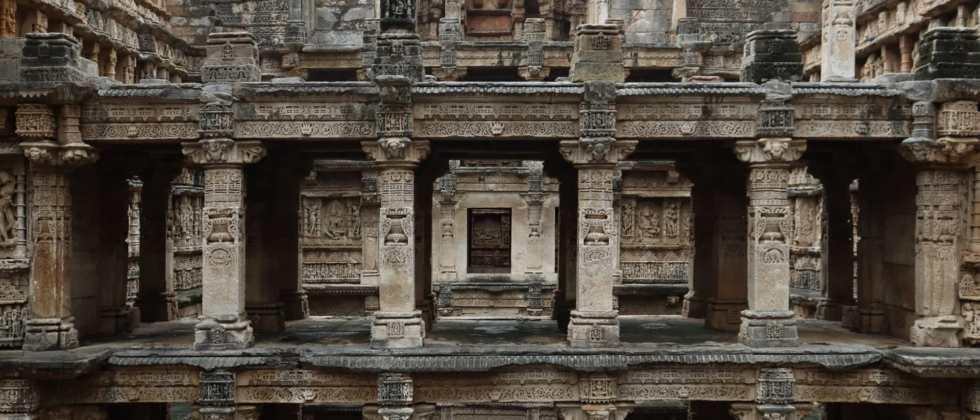 Carved stone terraces of an ancient stepwell descend level by level towards the water.