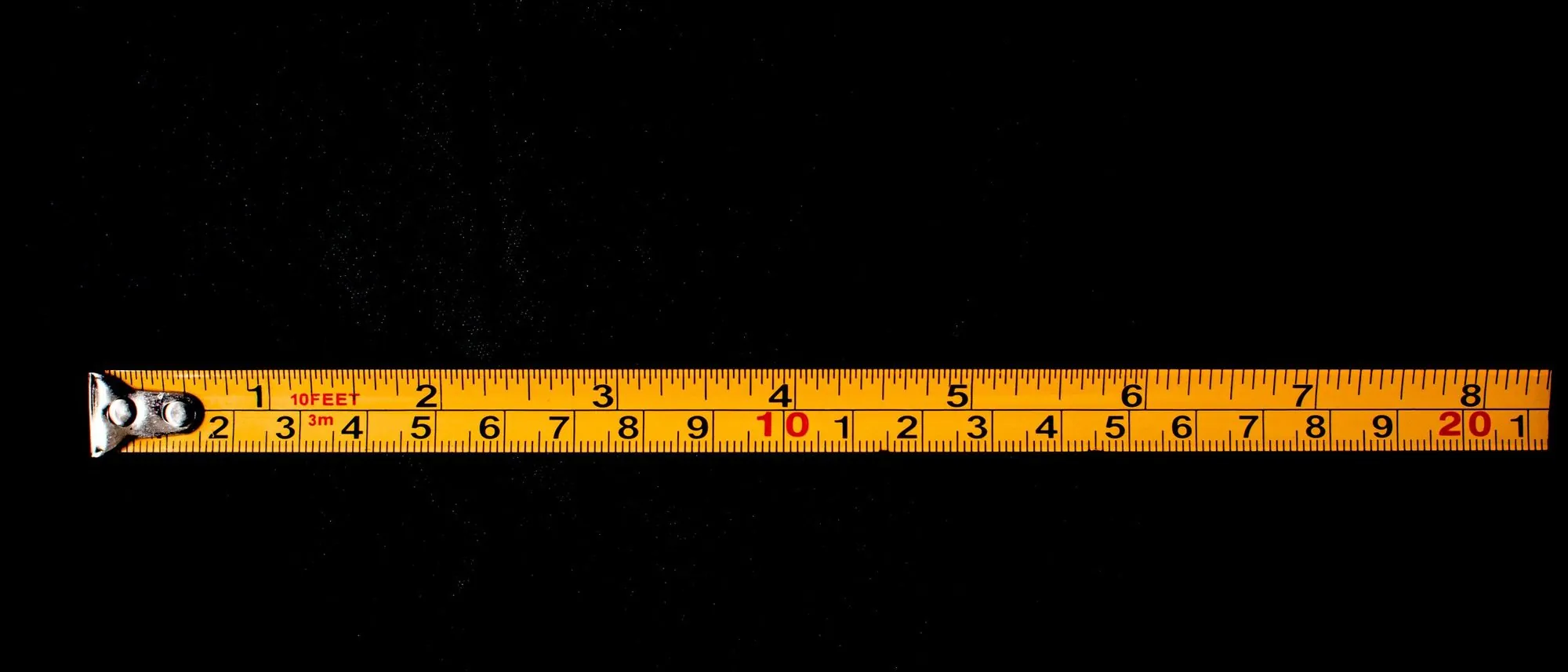 A yellow tape measure laid out across a black surface.
