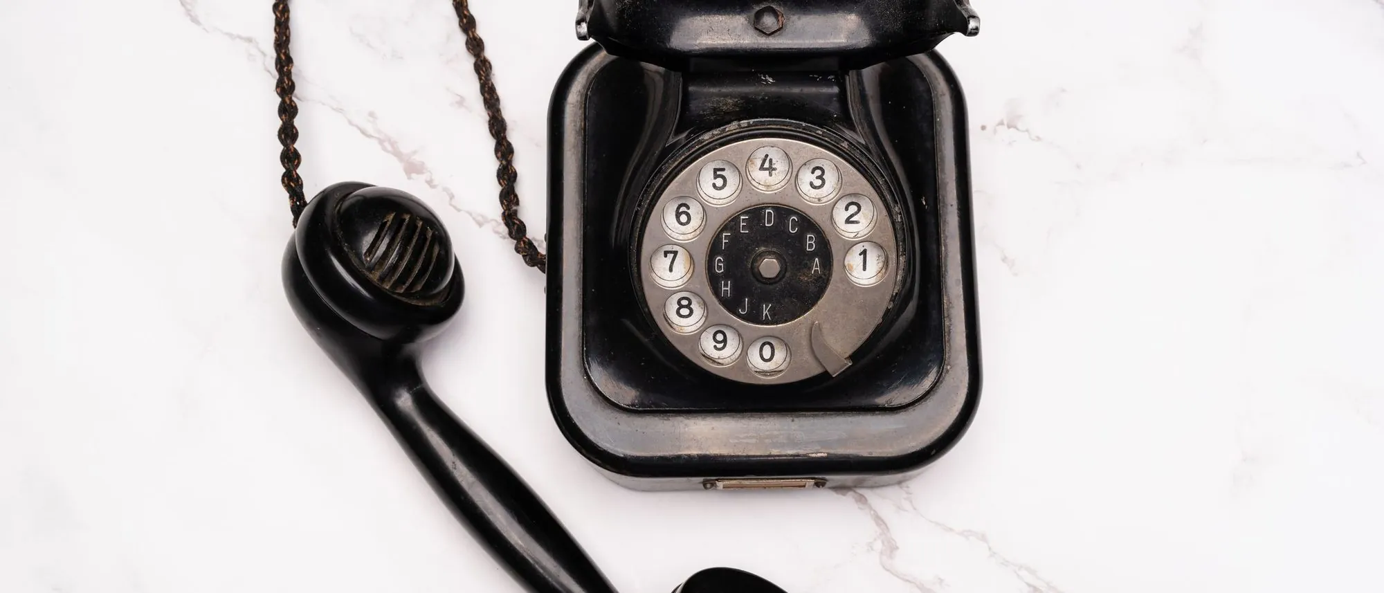 An old rotary dial telephone with its receiver rests on white marble.