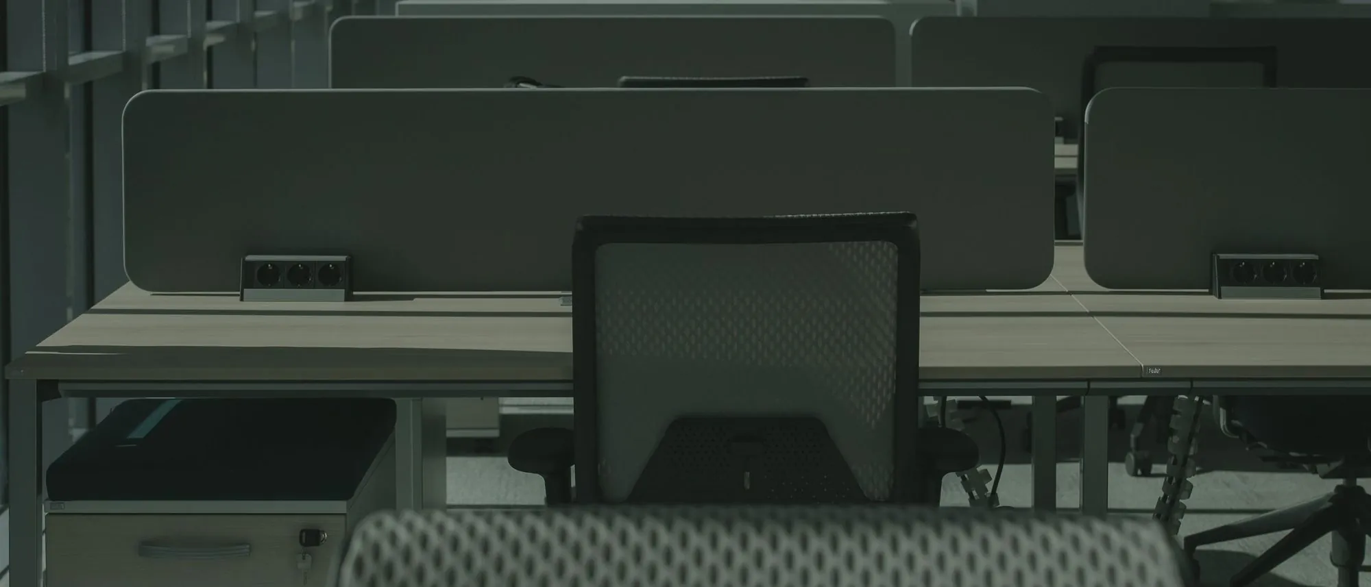 An office chair pushed back from an empty desk in a dim room