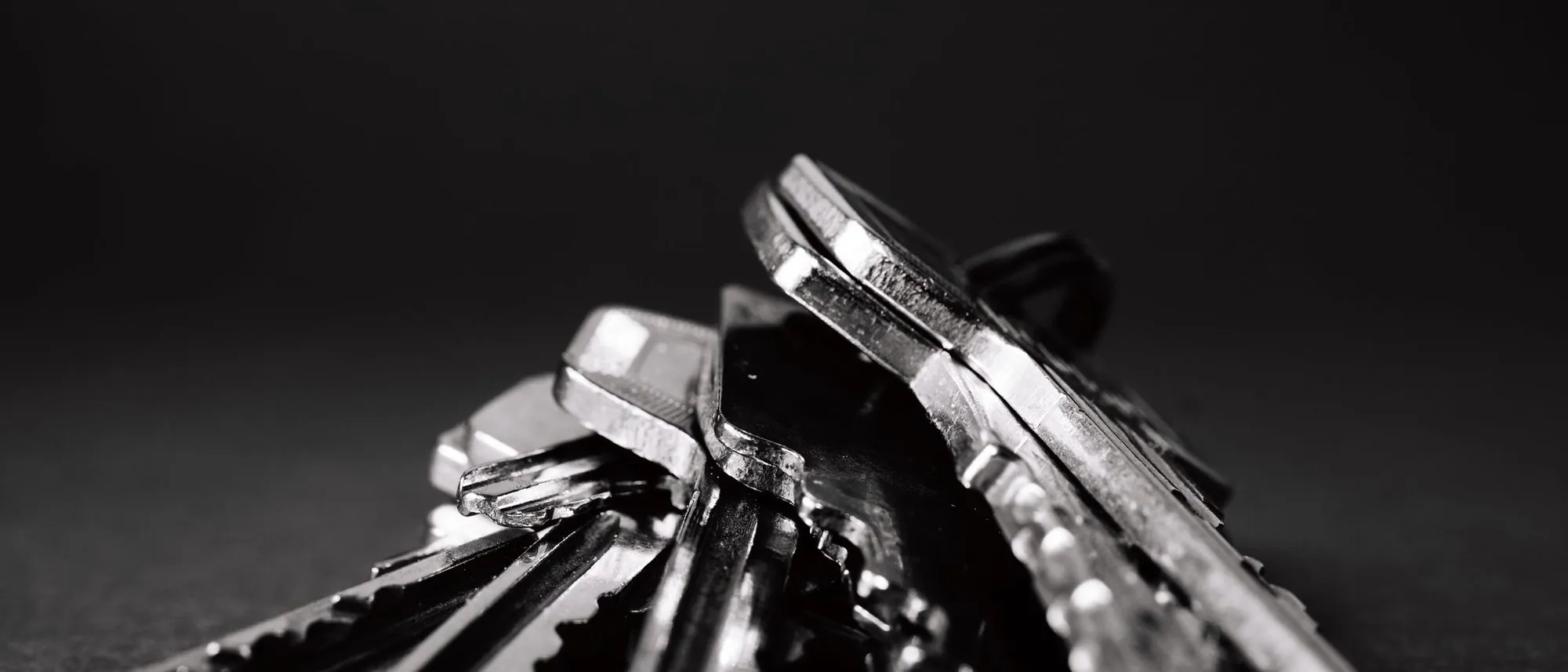 A pile of metal keys on a dark surface.