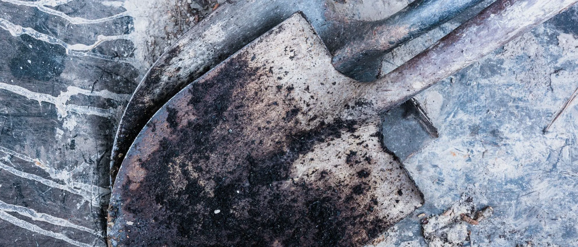Worn and rusted shovels lying on a concrete floor.