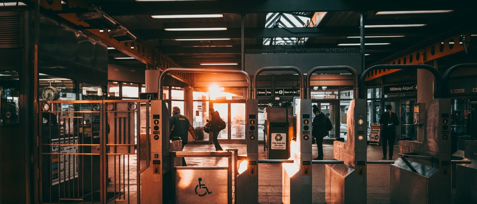 Ticket gates at a station entrance with low sunlight coming through from the platform side.