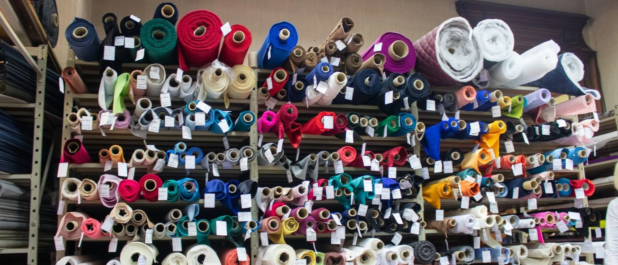 Rolls of fabric in many colours stacked on the shelves of a shop.