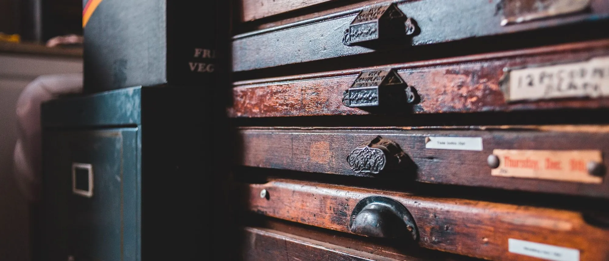An old wooden cabinet holds rows of narrow drawers with worn handles in a workshop.