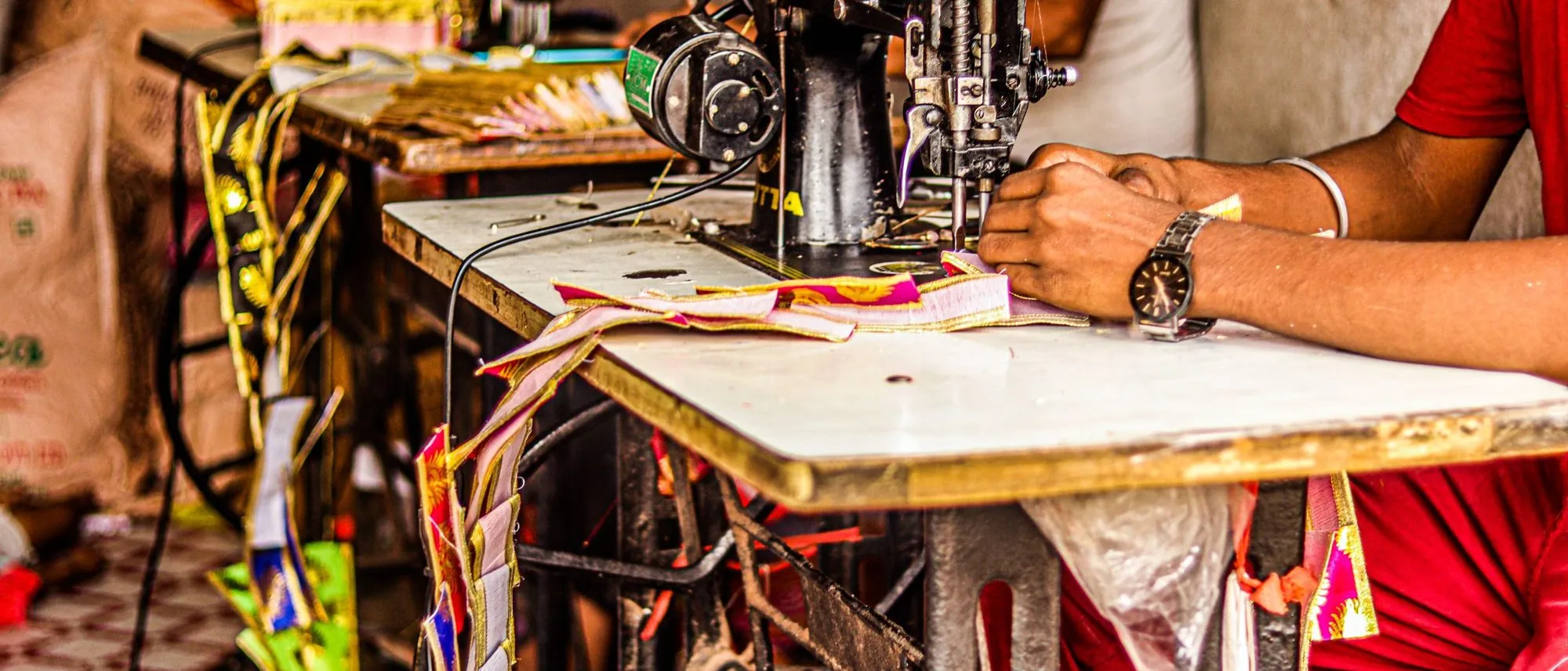 Close up, a tailor's hands guide bright fabric under the needle of an industrial sewing machine.