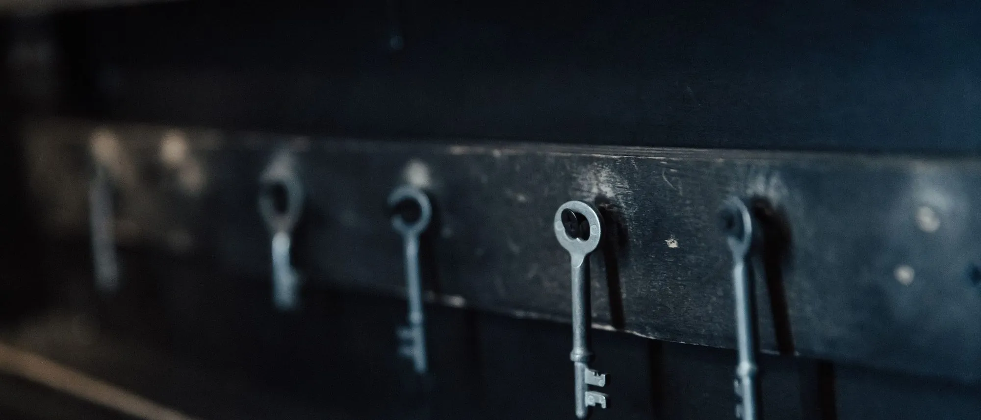 Antique metal keys hang in a row against a dark wall.