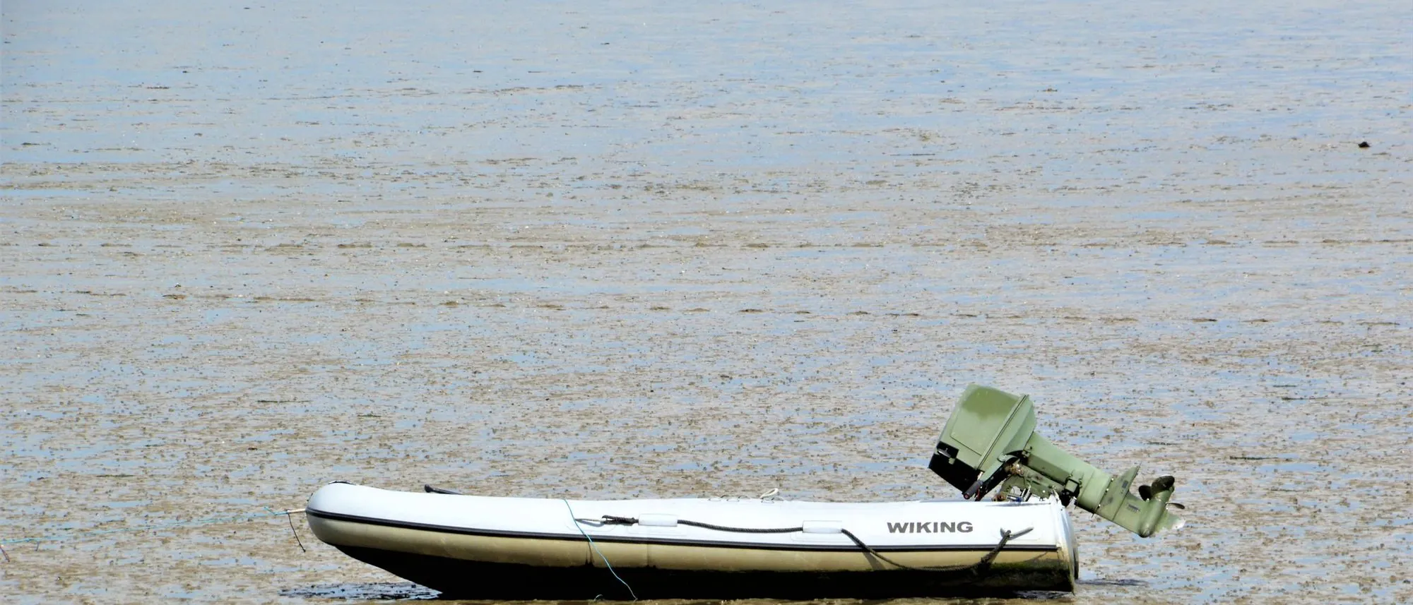 A small motorboat sits stranded on a tidal mudflat under a wide sky.