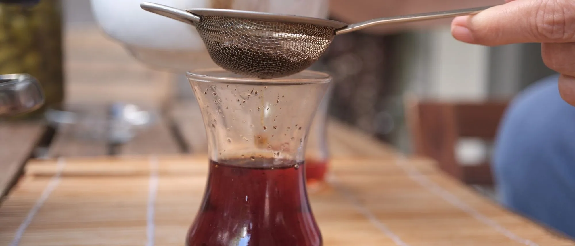 Tea is poured through a small strainer into a glass.