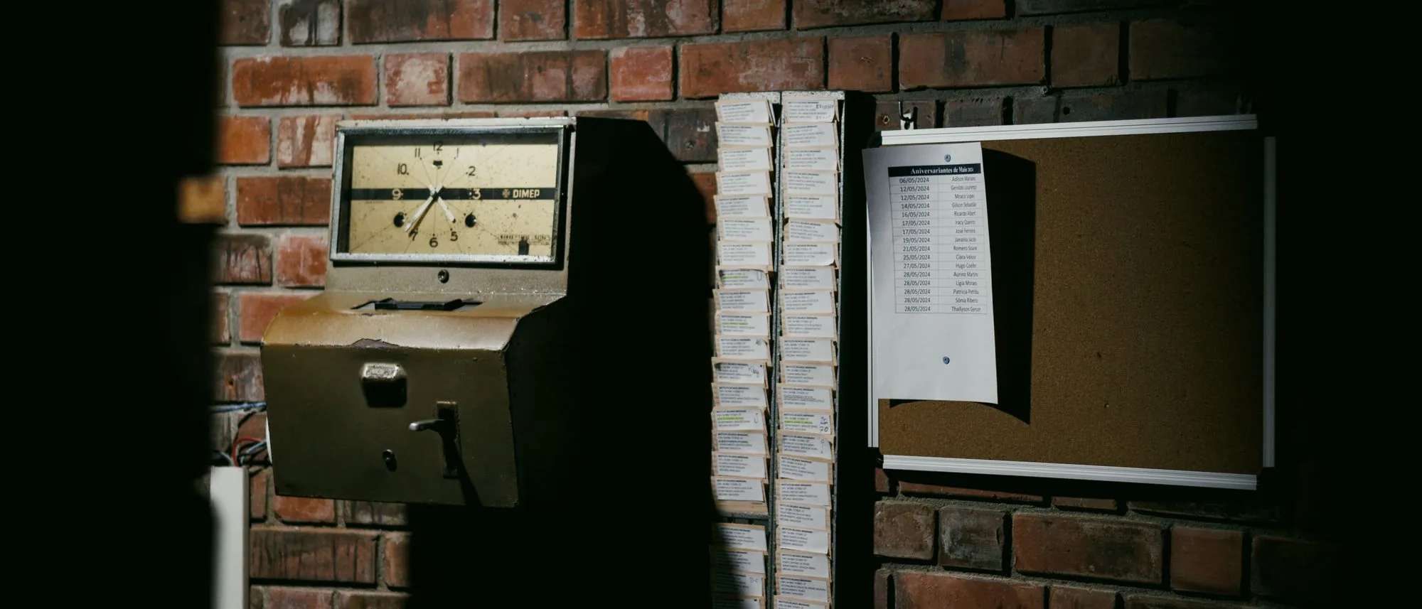 A retro punch-clock and rack of time cards on a dark brick wall