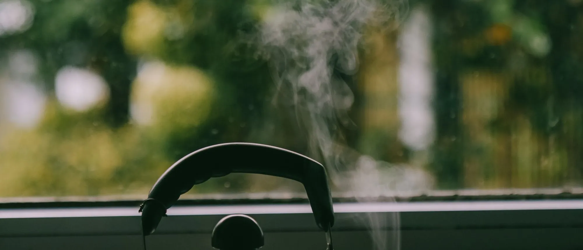 A steaming kettle on a windowsill against a soft green garden