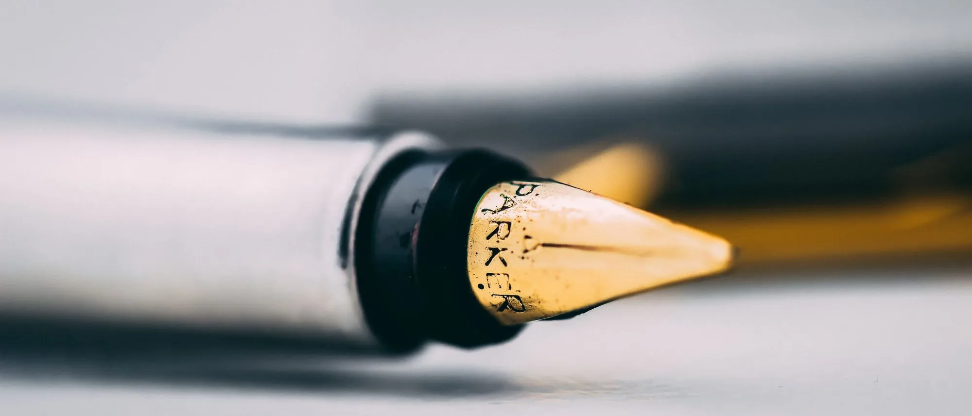 The nib of a fountain pen in sharp focus on a pale surface.
