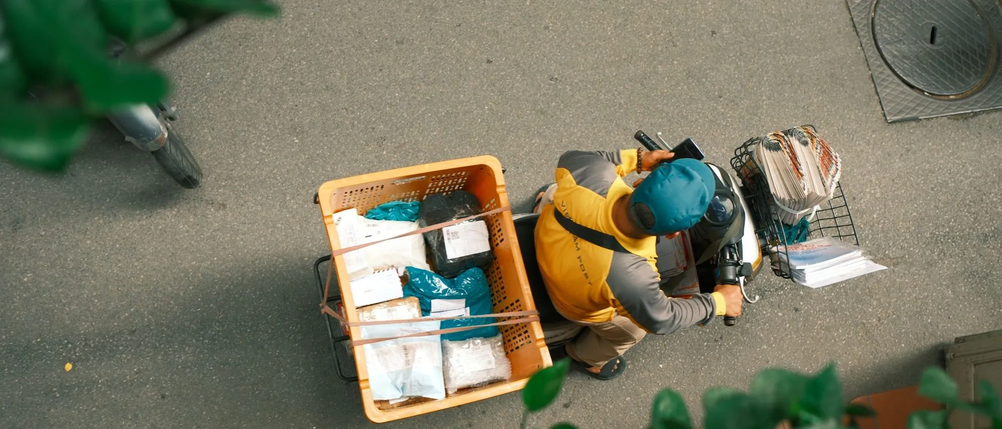Seen from above a courier on a scooter carries parcels along a sunlit street.