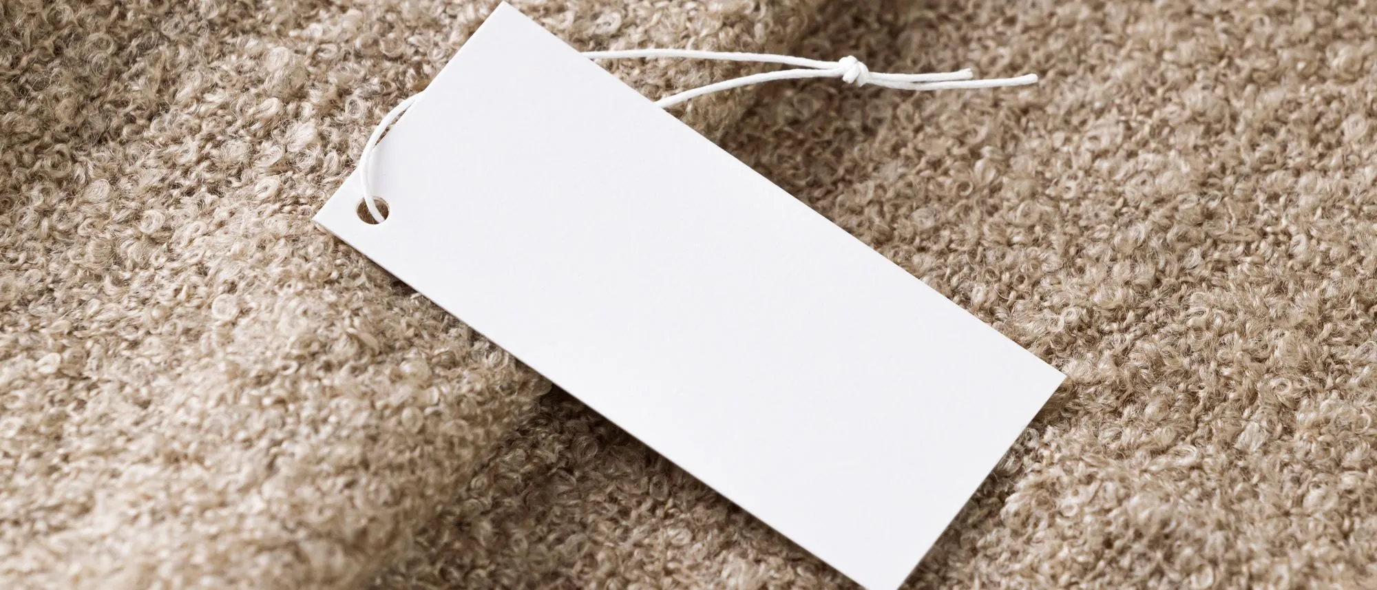 A blank white price tag on string lying on beige fabric