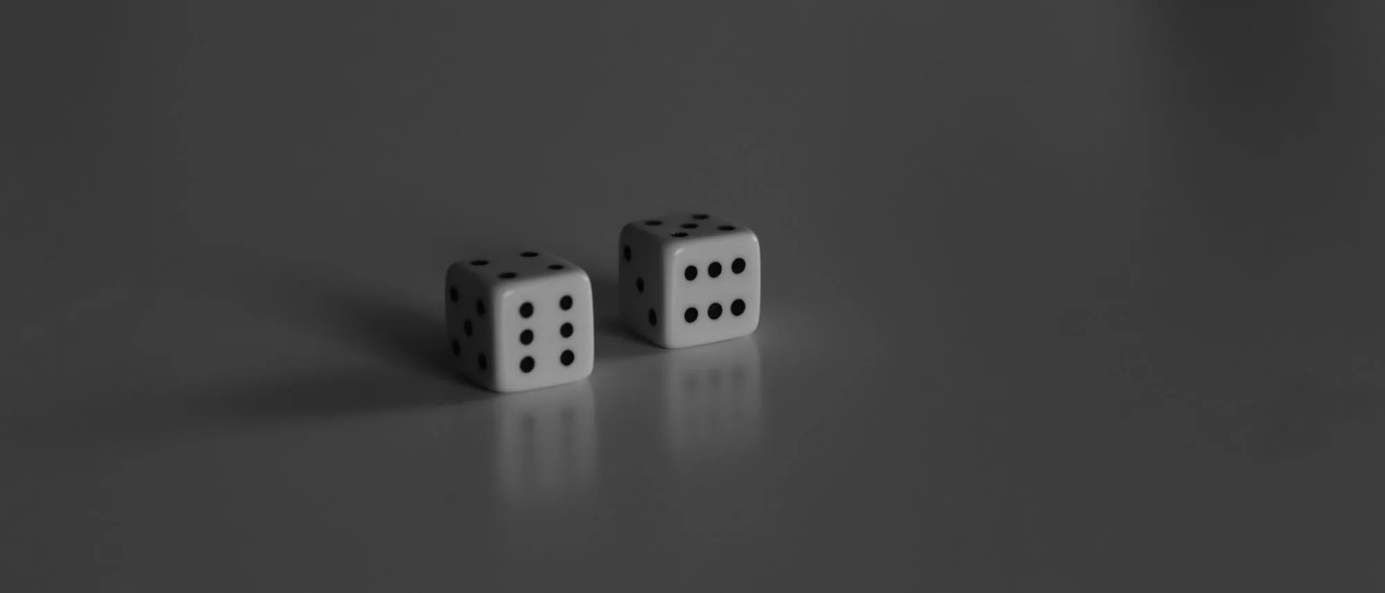 Two white dice standing on a grey reflective surface
