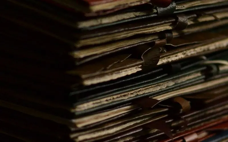 A tall stack of worn file folders tied with ribbon on a dark wooden desk