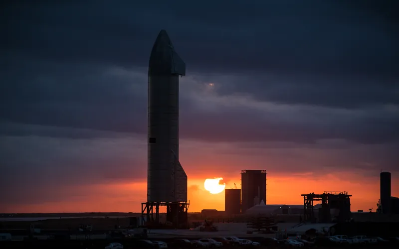 The silhouette of a Starship prototype against an orange sunset at Boca Chica in Texas