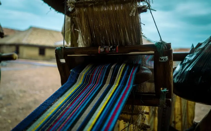 A handloom mid-weave with coloured threads stretched across the frame.