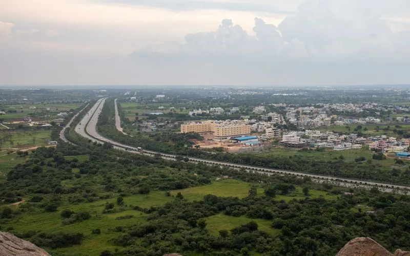 From the air a highway runs through green fields towards the edge of an Indian town.