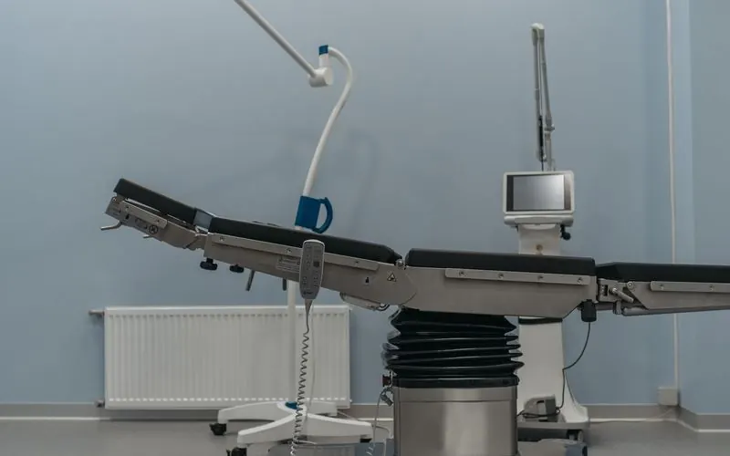 An empty operating table under a surgical lamp in a pale blue room