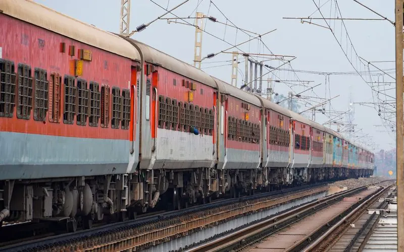 A long passenger train runs along elevated tracks in India.