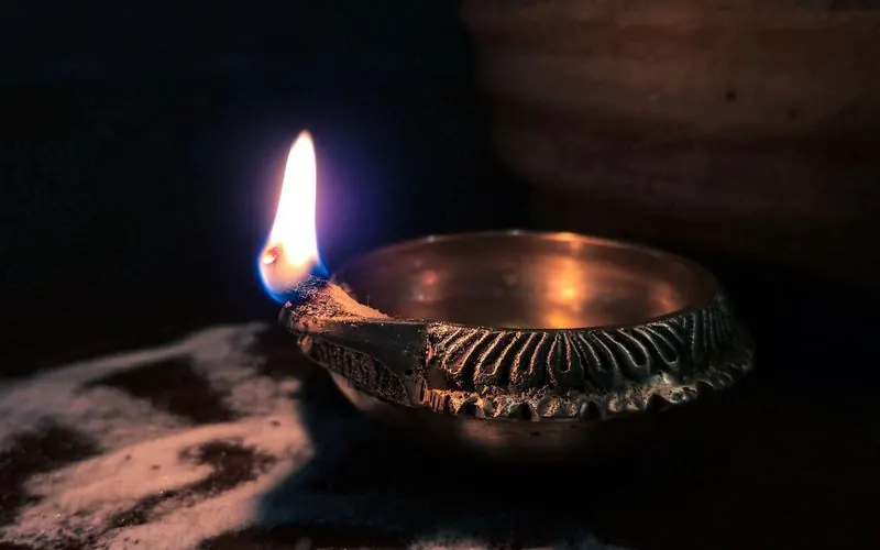 A single lit brass diya lamp on a dark floor