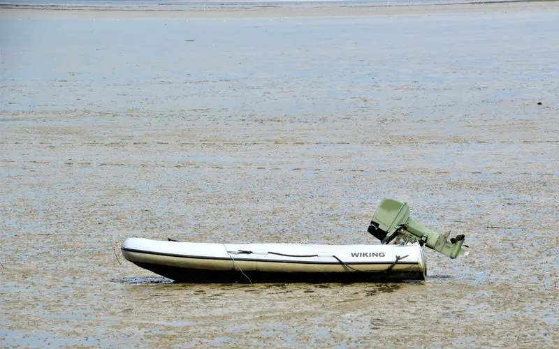 A small motorboat sits stranded on a tidal mudflat under a wide sky.