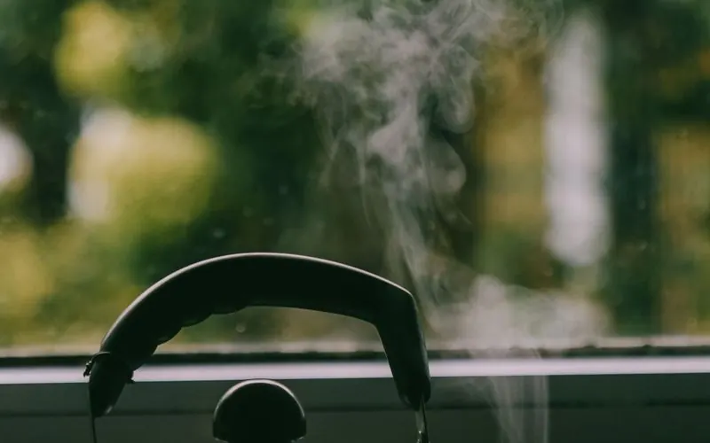 A steaming kettle on a windowsill against a soft green garden