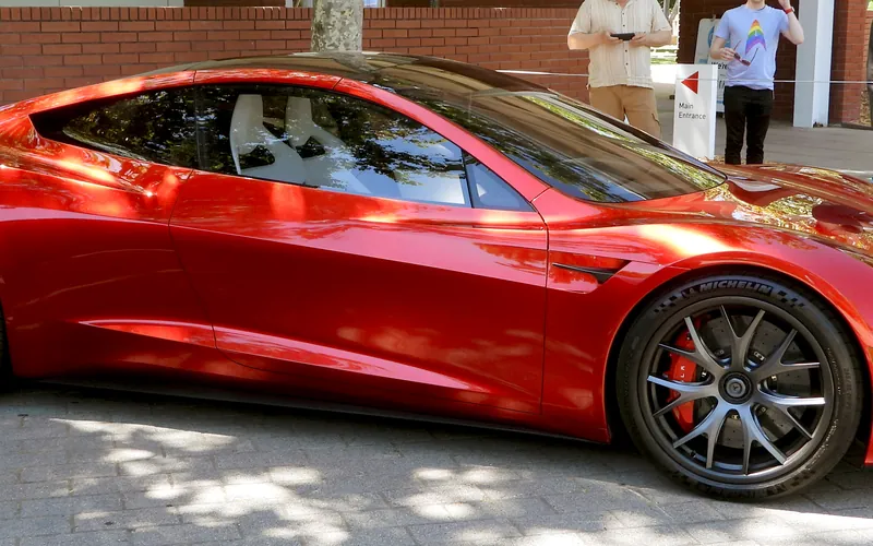 The red second-generation Tesla Roadster prototype parked on paving under trees