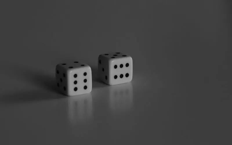 Two white dice standing on a grey reflective surface