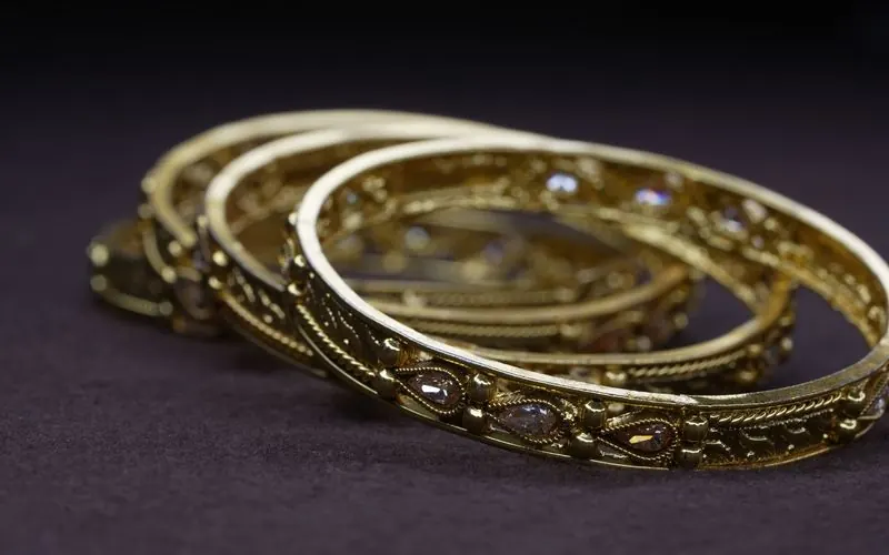Three gold bangles with fine filigree and small stones resting on a dark cloth