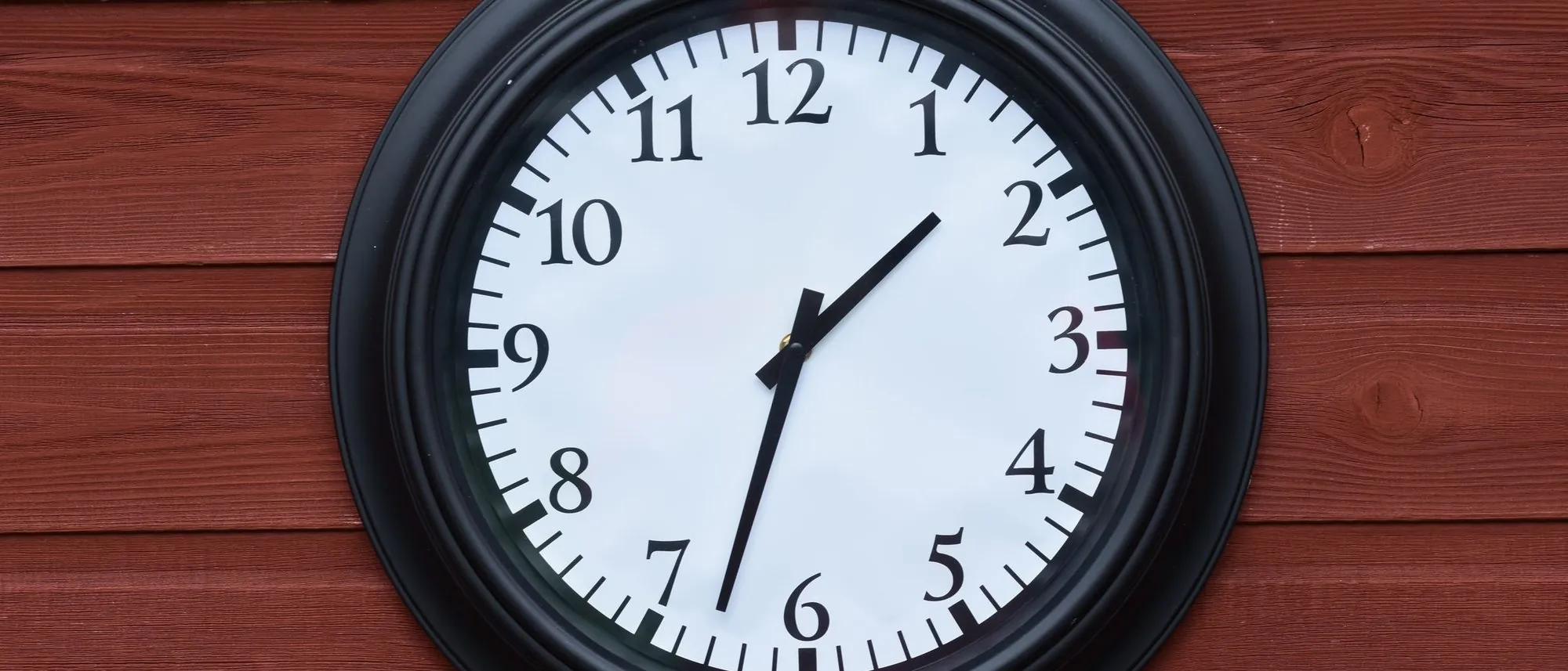 A plain black round clock hangs on a wall of weathered wooden planks.