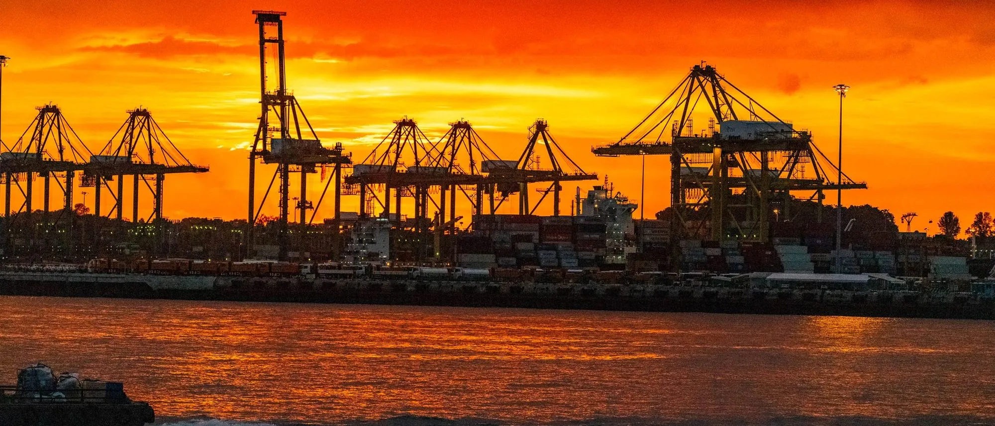 Harbour cranes in silhouette against an orange sky over the sea in Singapore.