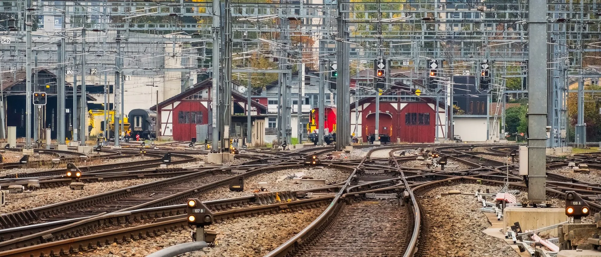 Several railway tracks running side by side past signals and buildings in daylight.