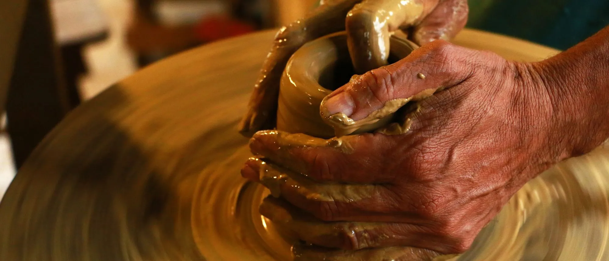 Hands shape wet clay on a spinning pottery wheel.